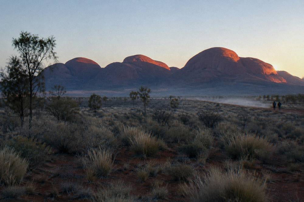 Sunrise light on the red domes of Kata Tjuta across open desert